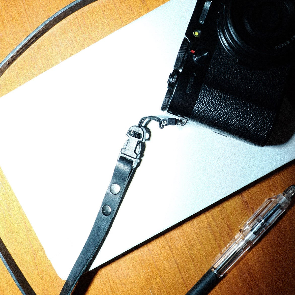 Camera with quick release camera strap on a wooden surface next to a pen