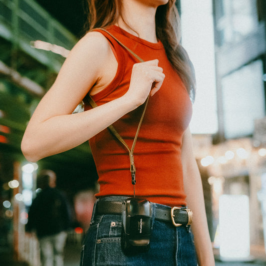 Woman wearing a red sleeveless top and blue jeans on a city street and carrying camera with quick-release camera strap