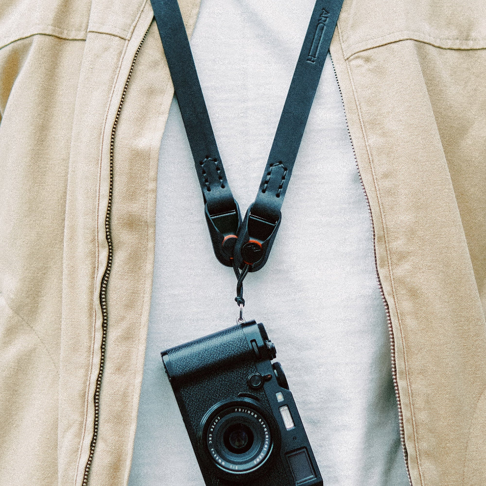 Camera with camera strap over a beige jacket on a light gray background