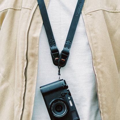 Camera with camera strap over a beige jacket on a light gray background