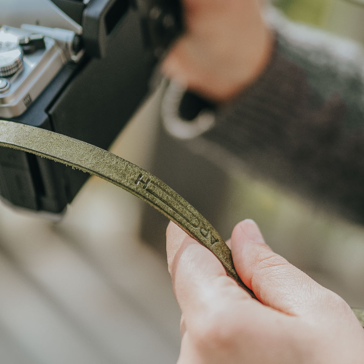 A person holdin Arch Appearance camera strap which is attached to the new OM SYSTEM OM-3 camera