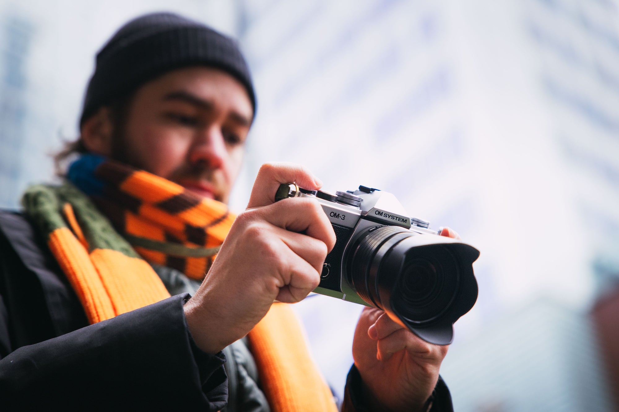 A man looking at his new OM SYSTEM OM-3 camera outdoors. The newly launched camera has also a new leather camera strap