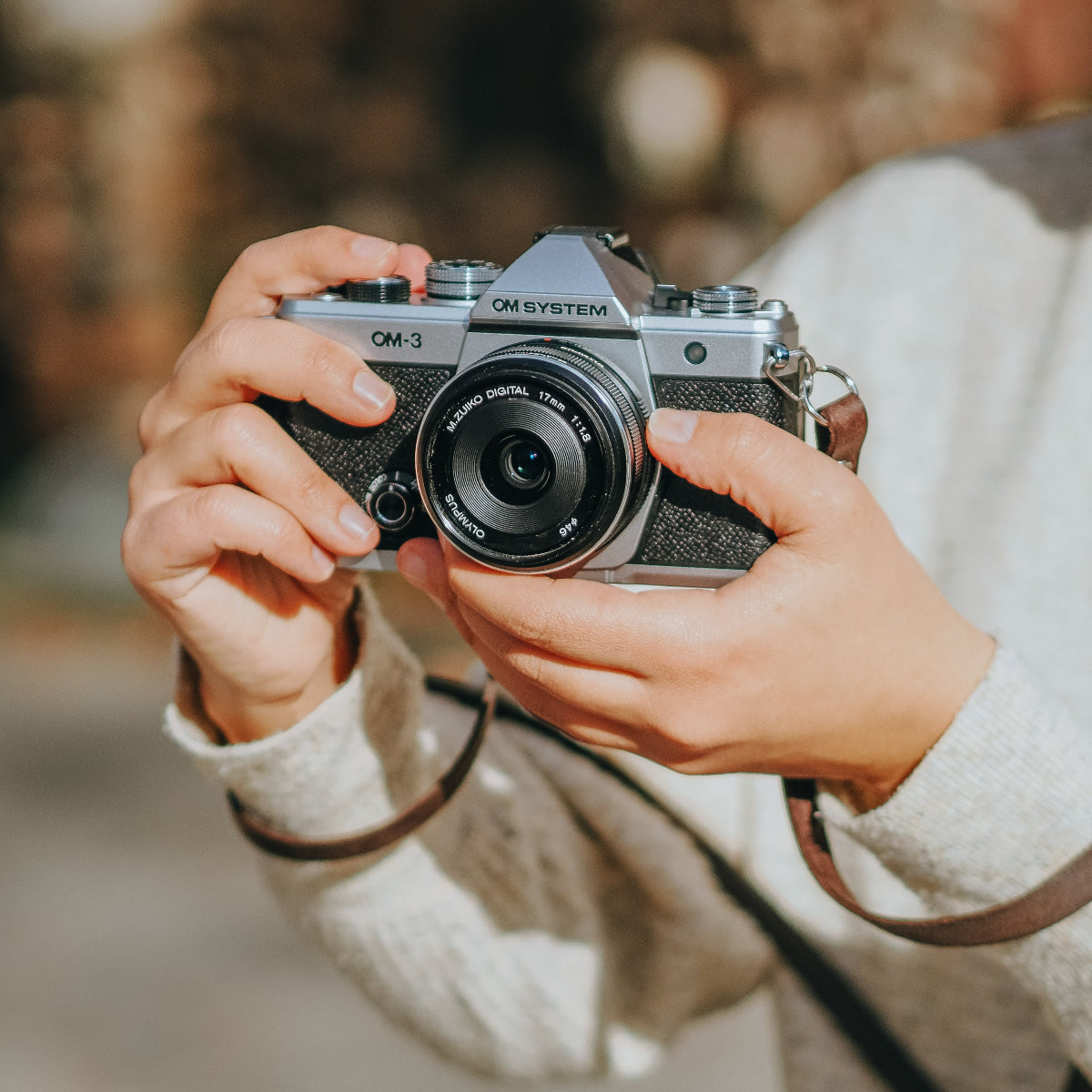 A person taking photos with the new OM SYSTEM OM-3 camera outdoors. A brown camera strap from Arch Appearance attached 