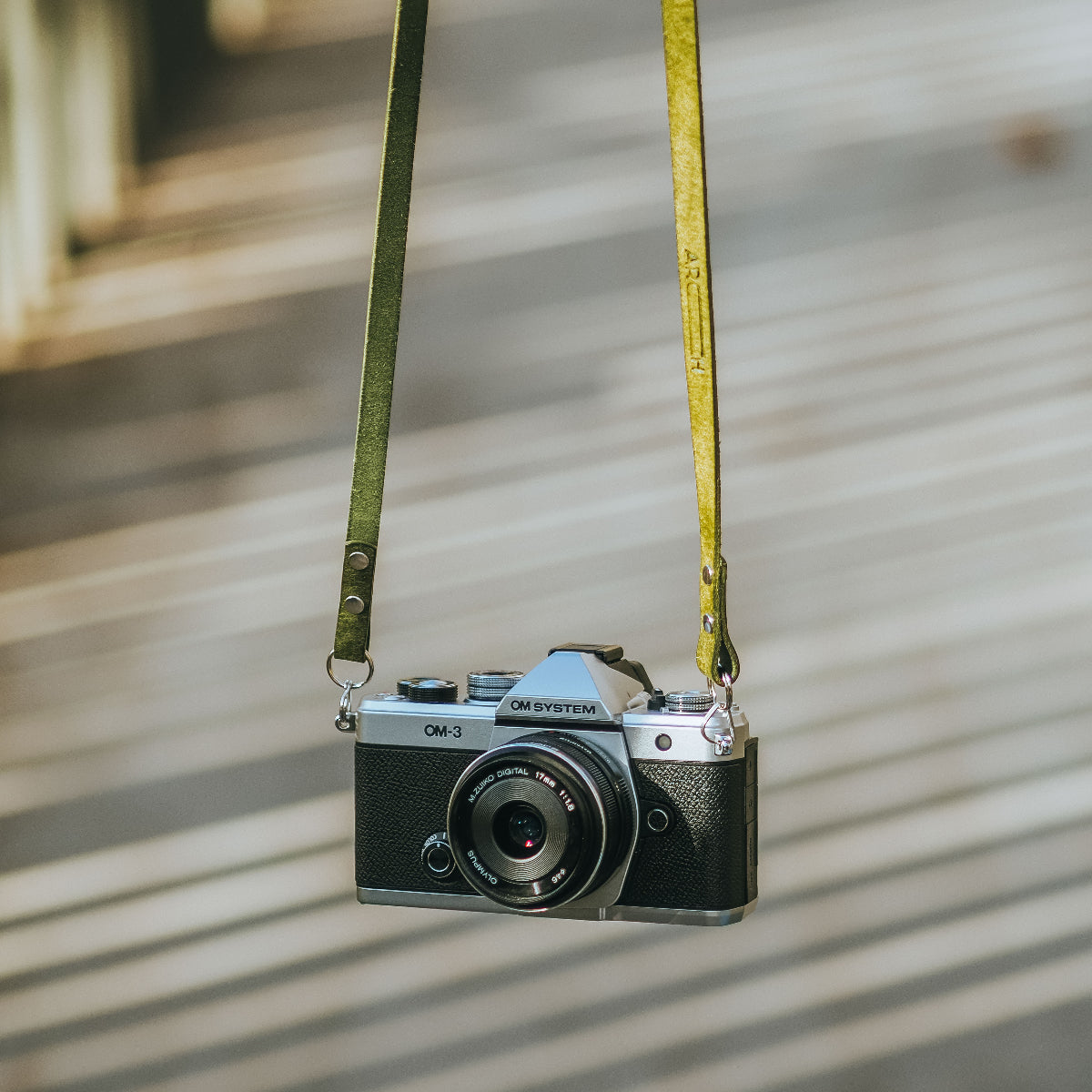 The new OM SYSTEM OM-3 camera hanging with olive green camera strap from Arch Appearance