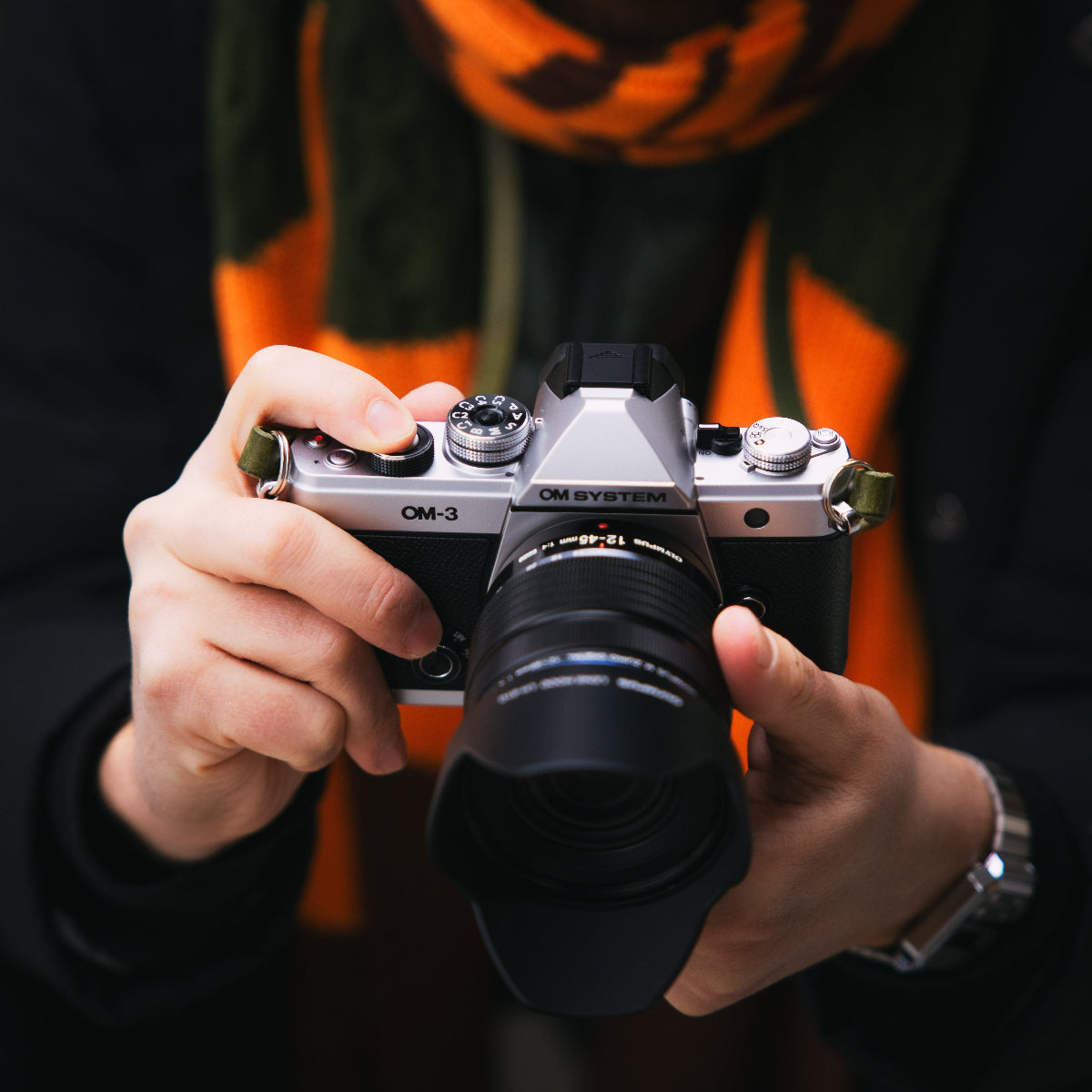 A man holding the new OM SYSTEM OM-3 camera with Arch Appearance camera strap in his hands