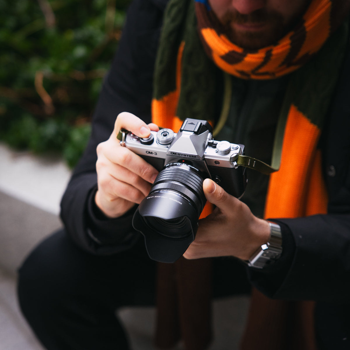 A man looking through photos from his new OM SYSTEM OM-3 camera which has also a new olive green leather camera strap on it