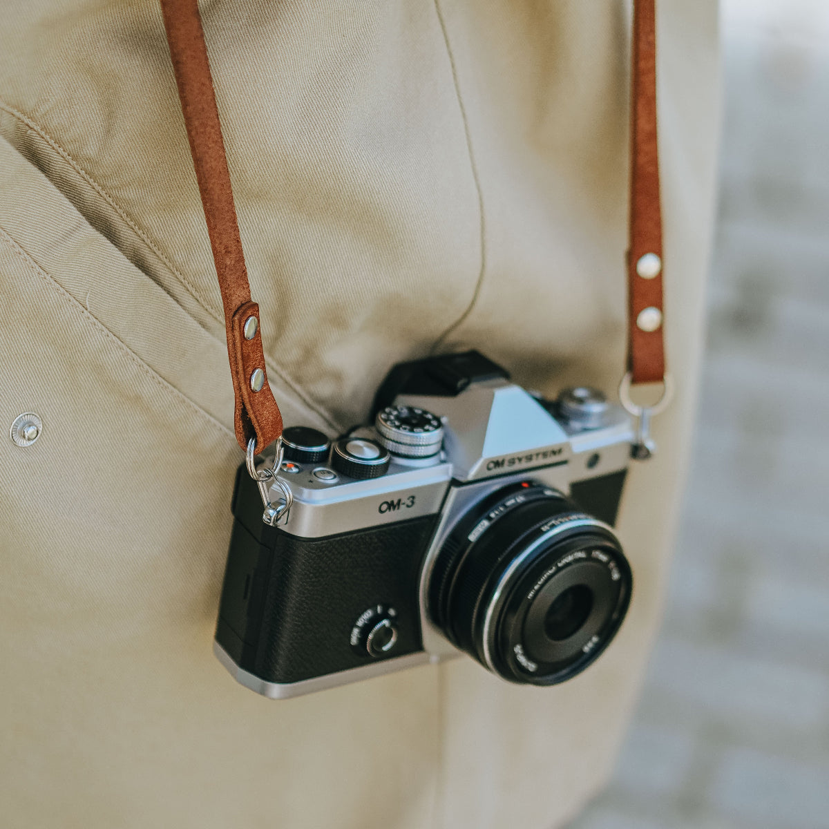 The new OM SYSTEM OM-3 camera displayed closely with a leather camera strap 