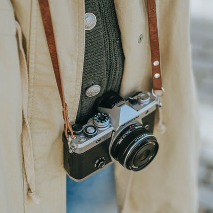 A person having the new OM SYSTEM OM-3 camera with walnut brown leather camera strap from Arch Appearance