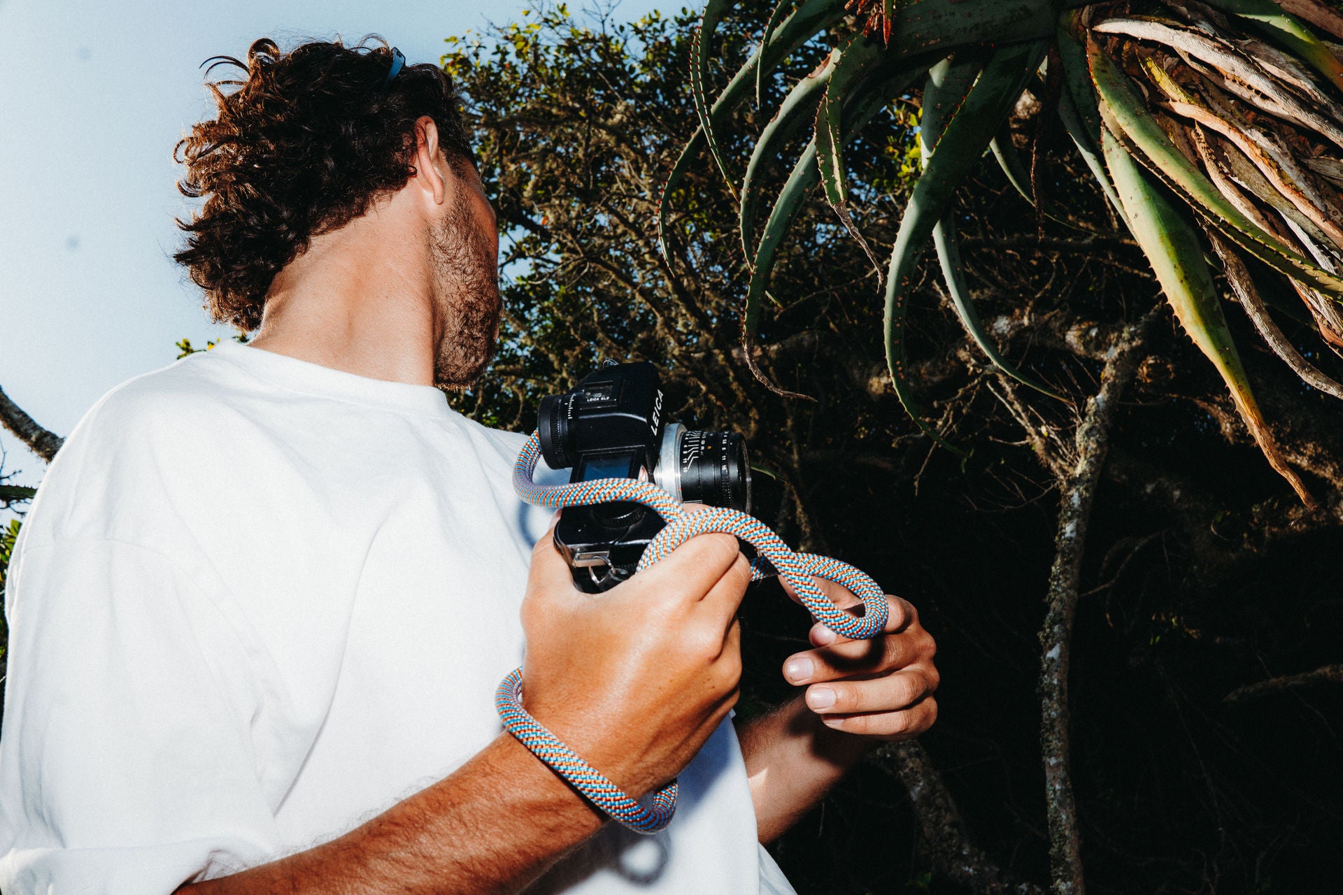 Person holding a camera and a rope camera strap with a natural background