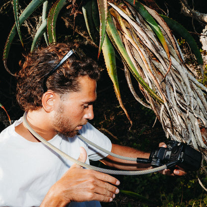 Person with a camera and rope camera strap in a natural setting