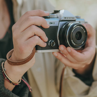 A person filming 4K video with the newly launched OM SYSTEM OM-3 camera which has walnut brown leather camera strap on it