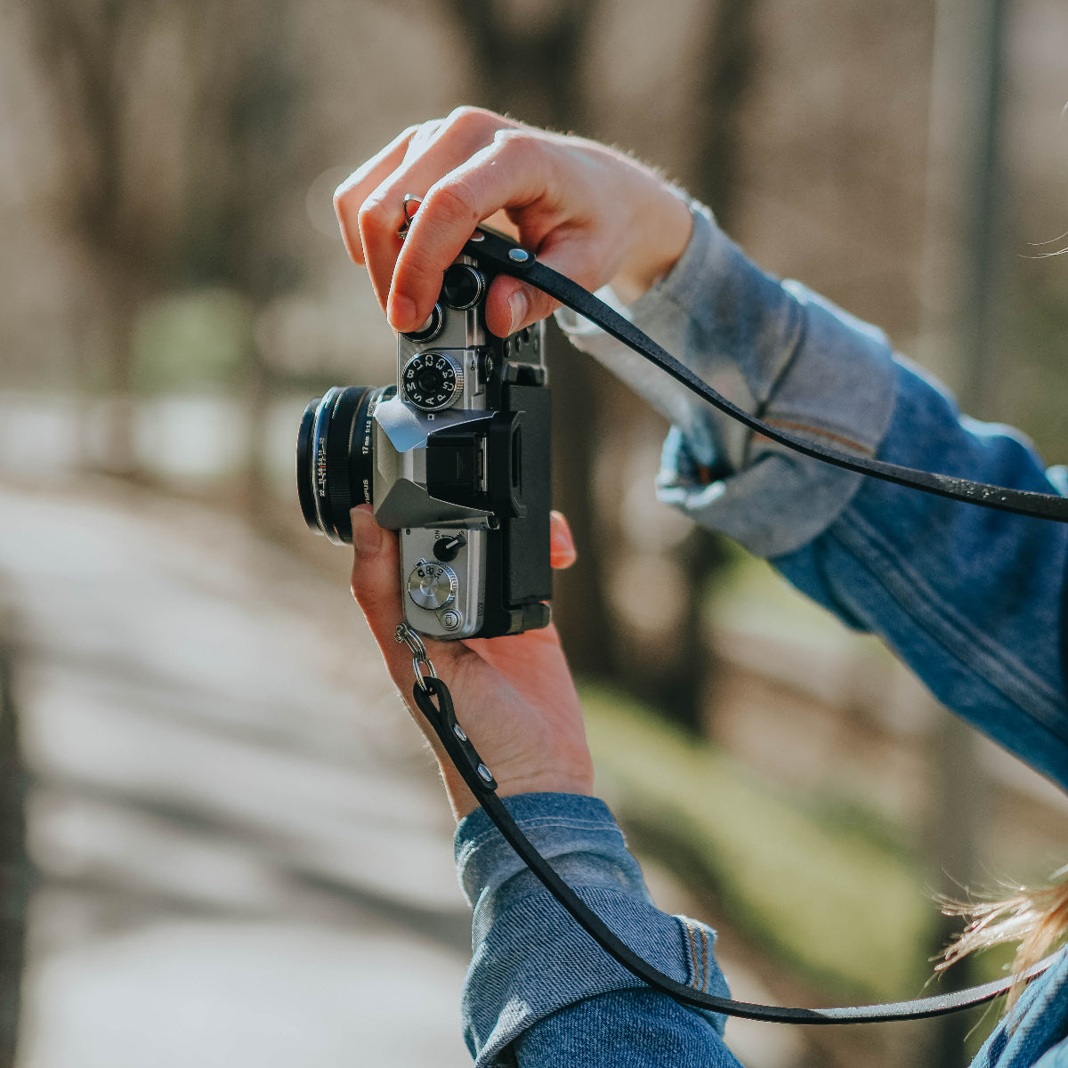 A person taking a photo vertically with the new OM SYSTEM OM-3 camera with black leather camera strap on